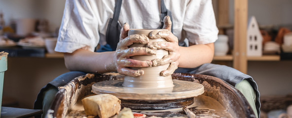 Potter working on a Potter's wheel making a vase. Young woman forming the clay with hands creating...