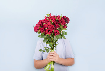 boy with a bouquet of red roses, portrait of a cute boy in a blue polo on a blue background, greeting and gift for Mother's day or Valentine's day
