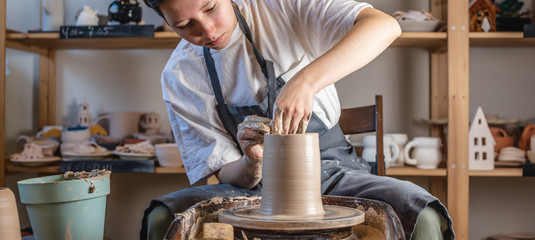 Potter working on a Potter's wheel making a vase. Young woman forming the clay with hands creating jug in a workshop.