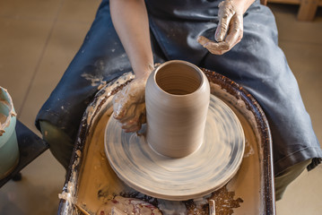Woman potter working on Potter's wheel making a vase. Master forming the clay with her hands creating jug in a workshop