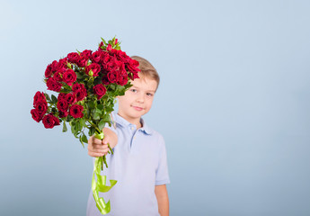boy with a bouquet of red roses, portrait of a cute boy in a blue polo on a blue background, greeting and gift for Mother's day or Valentine's day