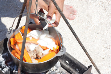 Fototapeta na wymiar Tourist cooking meat with vegetables in a cauldron on the beach.