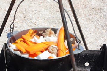 Tourist cooking meat with vegetables in a cauldron on the beach.