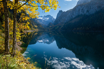 Fototapeta na wymiar Peaceful autumn Alps mountain lake with clear transparent water and reflections. Gosauseen or Vorderer Gosausee lake, Upper Austria. Dachstein summit and glacier in far.