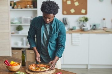 Fototapeta na wymiar Young African man standing in the kitchen and he is going to eat homemade pizza for lunch