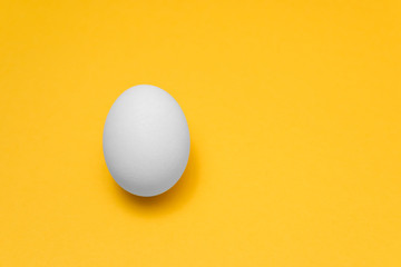 one white egg on yellow background on left side for designs, visual art for easter advertise