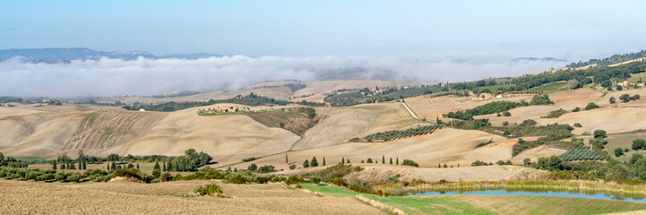 Beautiful foggy landscape in Tuscany - wave hills, cypresses trees, morning fog and clouds.