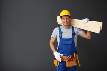 Handsome carpenter with wooden planks on dark background. Space for text