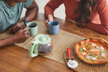 Close-up of young couple sitting at wooden table drinking coffee and eating pizza during lunch time