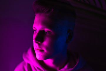 Young guy in a neon light. A teenager in a pink hoodie in trendy lighting of pink, purple and blue