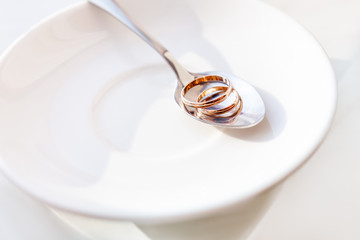 Golden wedding rings on shiny spoon. Traditional symbol of love and marriage on white plate.