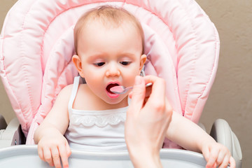 Feeding cute baby girl in pram with spoon