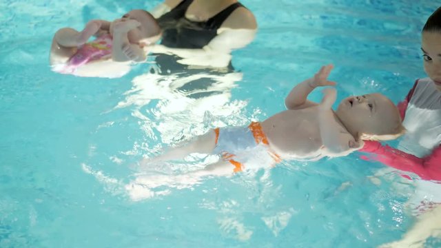 Swimming lesson. Mothers teaching to swim newborn baby at swimming pool