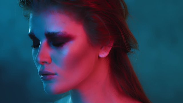 beautiful thoughtful redhead girl in neon lighting with trendy fashion makeup and hairstyle, neon light effect, blue and pink lighting, two colors