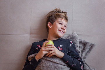 Above view of happy boy with an apple resting on sofa.