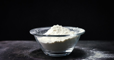 Flour is falling into a bowl in slow motion on black background