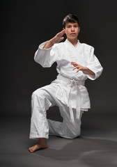 Fototapeta na wymiar portrait of a teenager dressed in martial arts clothing poses on a dark gray background, a sports concept