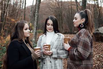 Portrait of beautiful brunette girls walking. Keeping takeaway drink in  hands. Smiling. Outdoors. Concept of fashion. Beautiful Teen Girls. Beautiful teen girls in trendy clothes.