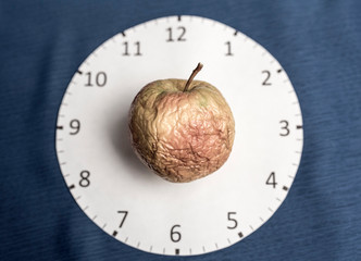 Clock face on a blue background and a wrinkled apple. Skin aging concept