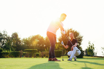 Young couple playing golf. Personal trainer giving lesson on golf course.
