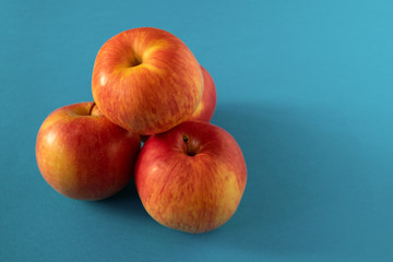 A few ripe yellow-red apples are piled up by a bunch on a blue background. View from the front. Horizontal orientation. Copy space.