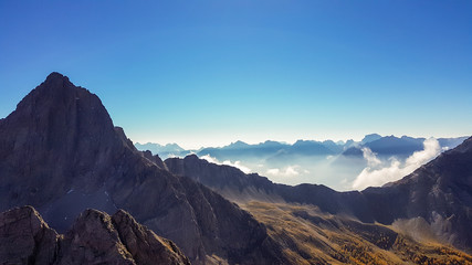 A panoramic view on Lienz Dolomites, Austria from the top of Grosse Gamswiesenspitze, bathing in the morning sun. The valley is shrouded in fog. High mountain climbing. Freedom and solitude