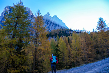 Fototapeta na wymiar A woman with big hiking backpack walking through a stony pathway to reach the Grosse Gamswiesenspitze in Lienz Dolomites, Austria. Sharp and barren slopes. Massive Alpine mountains. Solo wanderer