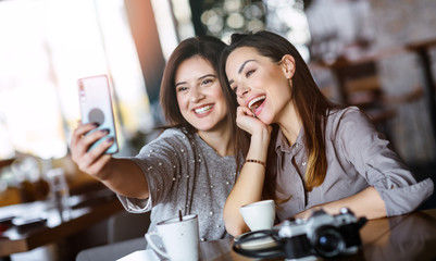 Image of young happy women friends sitting at cafe. Looking at camera make selfie.