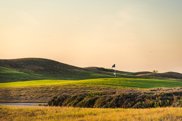 Fototapeta premium Golf club flag and green golf lawns at sunset.