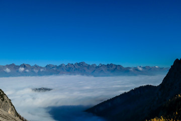Naklejka na ściany i meble A panoramic view on Lienz Dolomites, Austria from the top of Grosse Gamswiesenspitze, bathing in the morning sun. The valley is shrouded in fog. High mountain climbing. Freedom and solitude