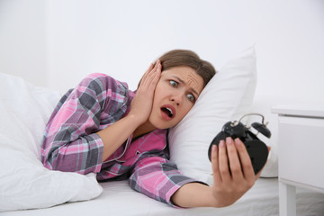 Emotional young woman with alarm clock at home in morning