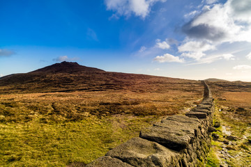 Fototapeta na wymiar Mourn Wall on the bank of Slieve Donard mountain with blue sky, white clouds and sunlight. Mourne Mountains range in Northern Ireland