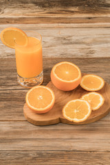 glass of fresh orange juice and oranges on cutting board
