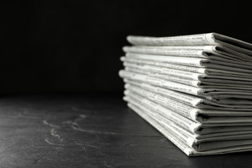 Stack of newspapers on dark stone table, space for text. Journalist's work