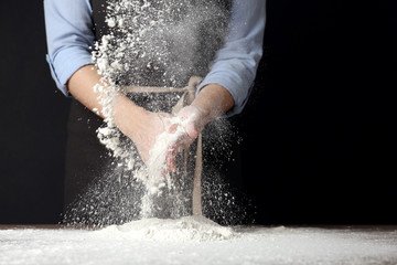 Woman working with flour at table against black background, closeup