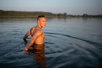 Athletic man on the lake. Waist-deep in water. On the Sunset.