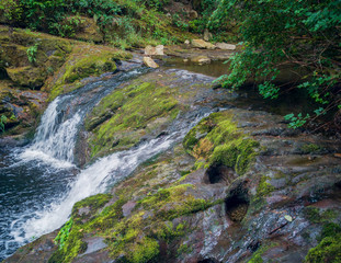 Fototapeta na wymiar Remarkable Lower Little Mashel Falls cascading into a moss covered rocky surface leading to a small pool of water in the creek at the Charles Pack Forest during the summer in Pierce County Washington 