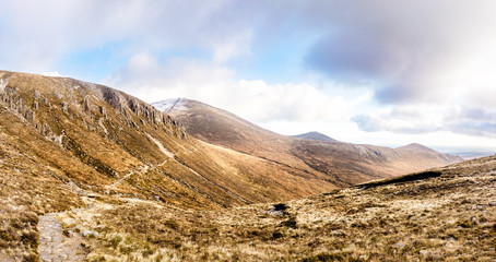 Fototapeta premium Footpath leading to snow capped peak of Slieve Donard mountain. Mourn Wall surrounding Mourn Mountains, highest range in Northern Ireland