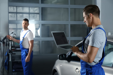 Fototapeta na wymiar Mechanic with laptop doing car diagnostic at automobile repair shop. Space for text