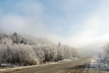 Obraz na płótnie Canvas The road to the mountains. Winter landscape with a mountain road in the morning fog. In the early foggy morning, the road to the mountains looks especially mysterious and beautiful. 