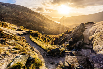 Footpath and large boulder leading to valley with water reservoir, dramatic sunset with sunrays....