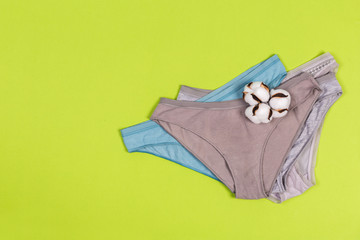 Female pastel cotton set panties and cotton flower on green background top view flat lay with copy space for text. shopping concept.