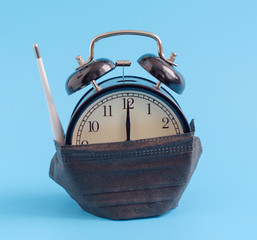 alarm clock in a protective respiratory mask and a thermometer on a blue background, concept of...