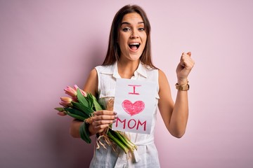 Beautiful woman celebrating mothers day holding love mom message and bouquet of tulips screaming proud and celebrating victory and success very excited, cheering emotion