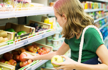 Pretty little girl choosing apples in the supermarket.