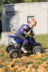 Obraz na płótnie Canvas The little girl rides a quad bike ATV race. A mini quad bike is a cool girl in a helmet and protective clothing. Electric quad bike electric car for children popularizes green technology.