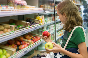 Pretty little girl choosing apples in the supermarket.