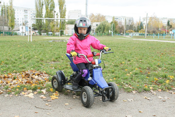 The little girl rides a ATV quad bike. A mini quad bike is a cool girl in a helmet and protective clothing. Electric quad bike electric car for children popularizes green technology.