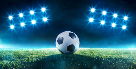 Soccer ball on a football field backlit by floodlight