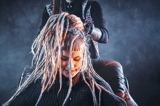 Young pensive woman got new freaky hairstyle from dreadlocks master.